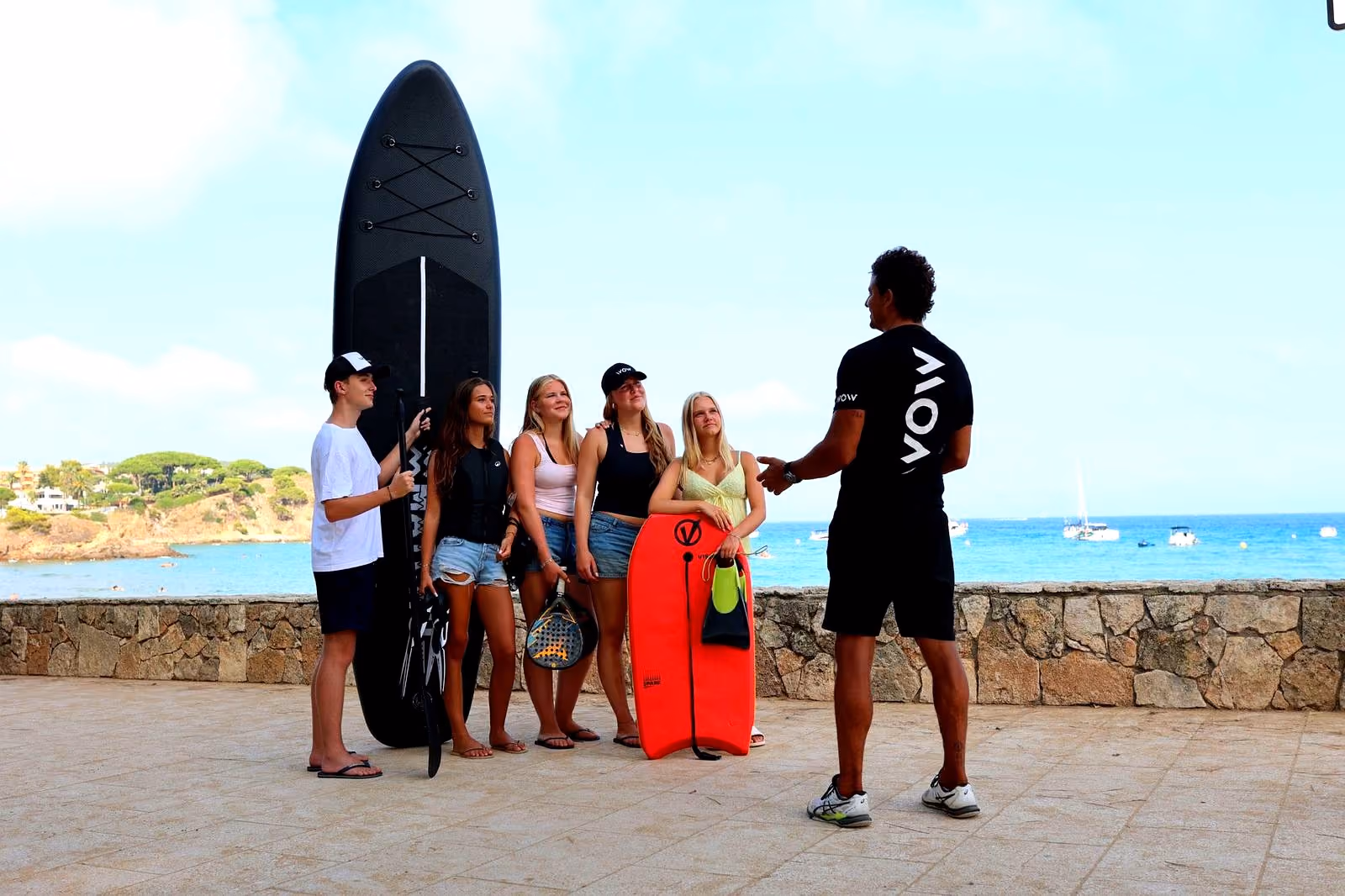 WOW-instructeur geeft scholieren uitleg bij SUP, bodyboard en padelracket in Palamós, Spanje